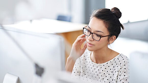 woman in white polka dotted shirt sitting at computer woman in white polka dotted shirt sitting at computer with glasses on researching women in workplace initiatives