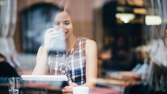 woman in coffee shop researching information about women in the workplace on a tablet