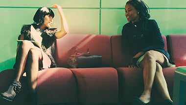 Two women sitting on a red couch discussing negotiation strategies